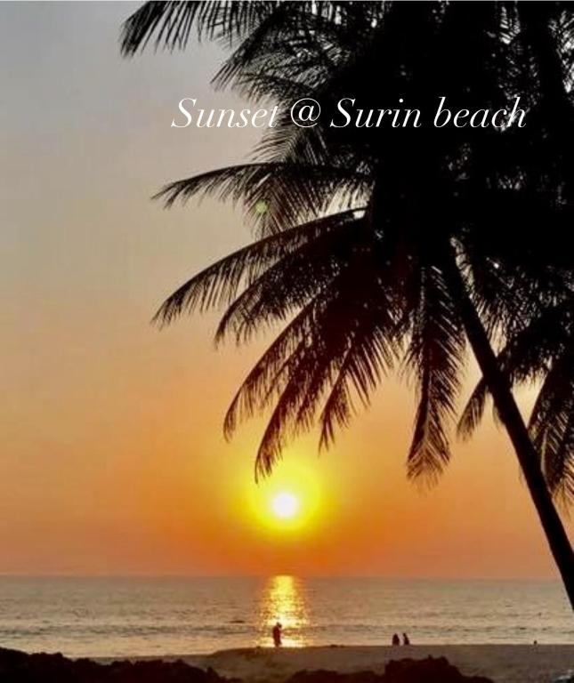 a sunset on the beach with a palm tree at Surin Bay Inn in Surin Beach