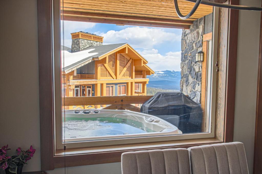 a window with a view of a house with a hot tub at Stonegate Resort Unit B208 in Big White