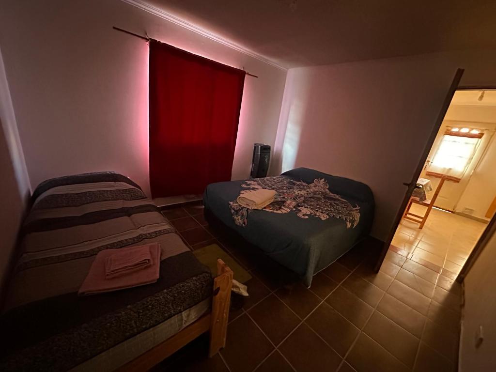Habitación pequeña con 2 camas y cortina roja. en Hospedaje al Fondo, en Gobernador Gregores