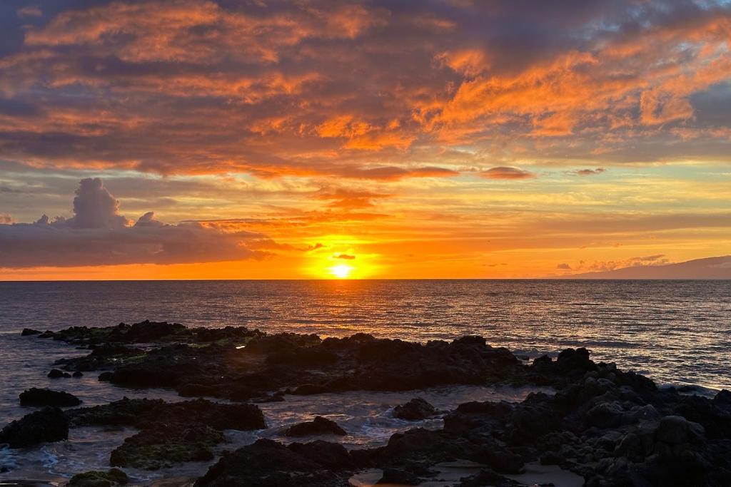 a sunset over the ocean with rocks in the water at Menehune Shores 606 - Direct Ocean Front, Split AC in Kihei