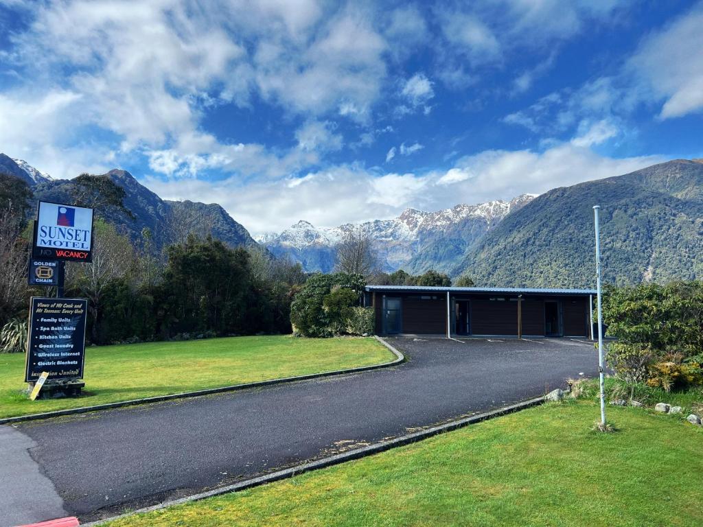 a road leading to a building with mountains in the background at Sunset Motel in Fox Glacier