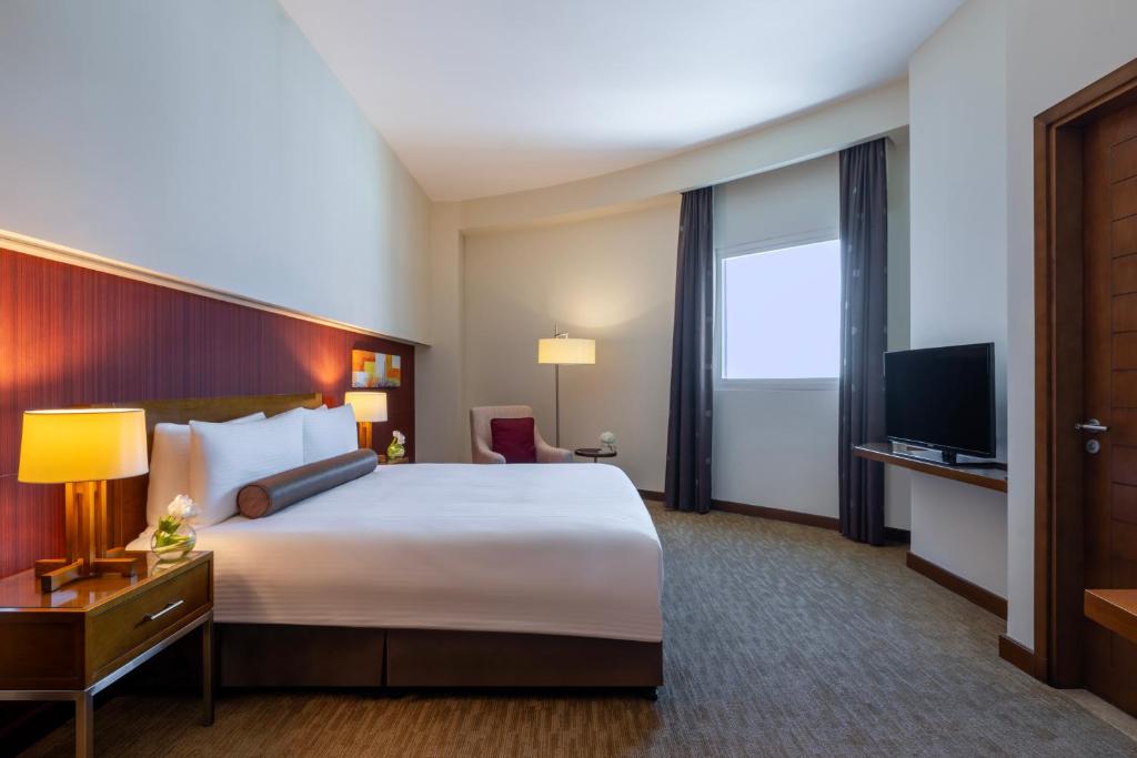 a hotel room with a large bed and a television at Grand Millennium Al Wahda Hotel and Executive Apartments Abu Dhabi in Abu Dhabi