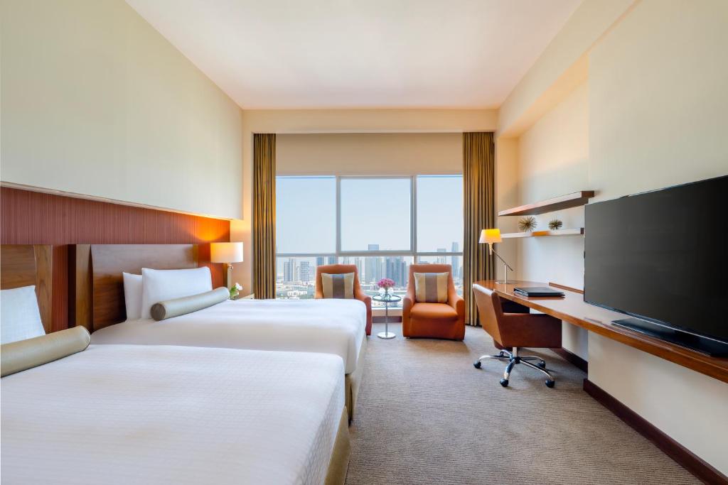 a hotel room with two beds and a flat screen tv at Grand Millennium Al Wahda Hotel and Executive Apartments Abu Dhabi in Abu Dhabi