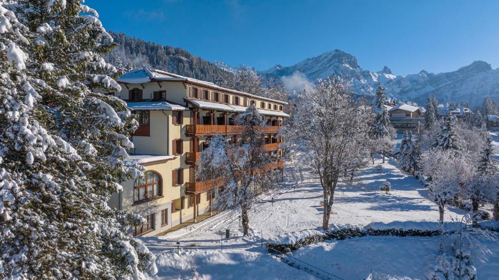 a building covered in snow with trees and mountains at Villars Lodge in Villars-sur-Ollon