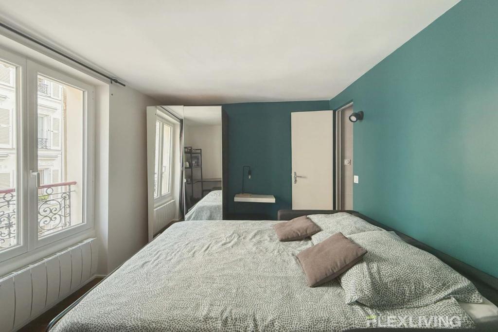 une chambre avec un lit avec un mur bleu dans l'établissement Flexliving - Studio - Martyrs, à Paris