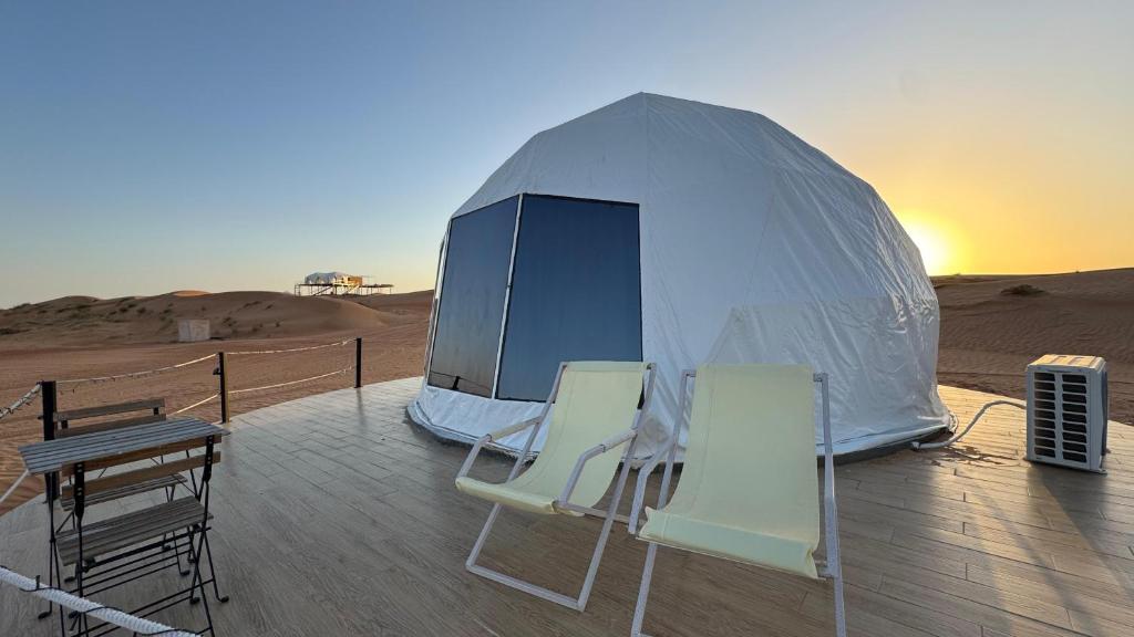 una tenda nel deserto con sedie e tavolo di Starry Domes Desert Camp a Badīyah