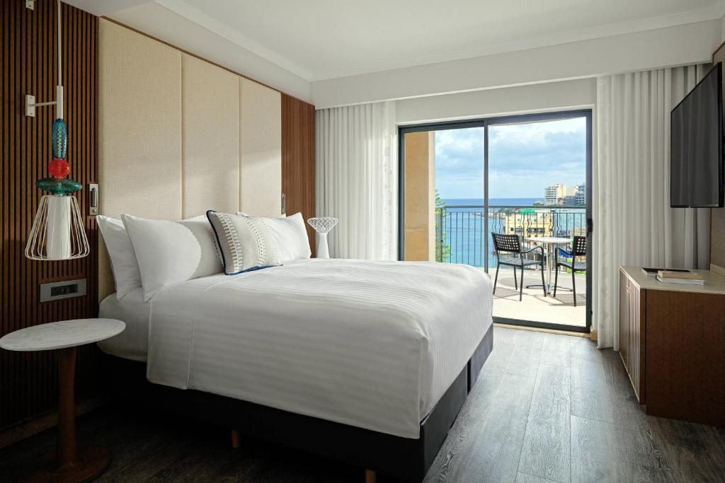 a hotel room with a large bed and a balcony at Malta Marriott Resort & Spa in St. Julianʼs