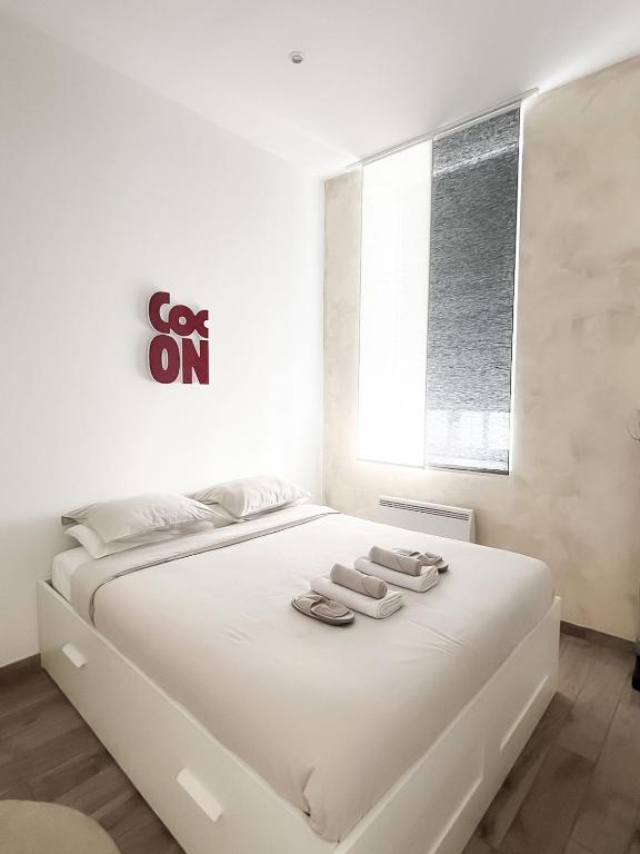 a white bedroom with a white bed with two slippers at Le Petit Cocon - Pause douceur in Cambrai