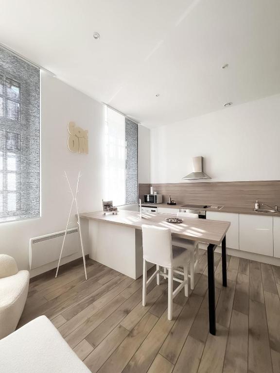 a white kitchen with a wooden table and white chairs at Le Petit Cocon - Pause douceur in Cambrai