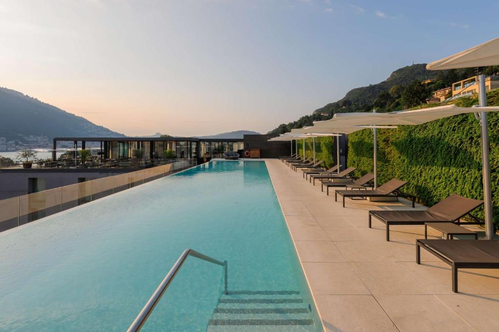a swimming pool with chairs and umbrellas on a building at Hilton Lake Como in Como