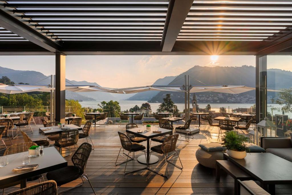 a restaurant with tables and chairs and a view of the mountains at Hilton Lake Como in Como