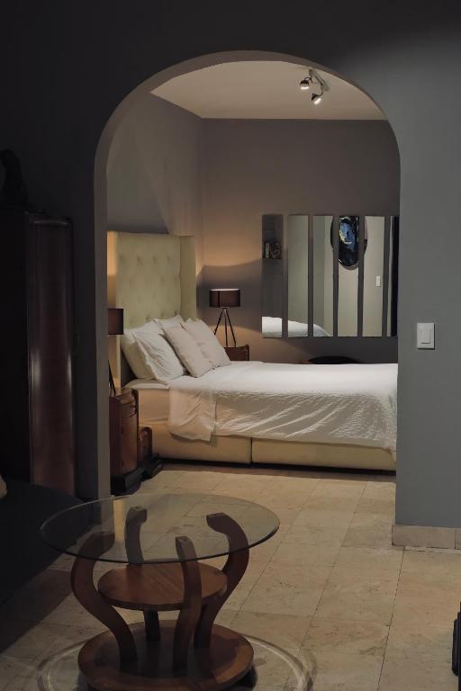An arched doorway opens onto a bedroom with a tufted headboard and glass coffee table.
