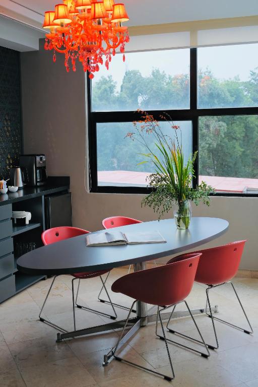 A bright dining table with red chairs faces a leafy view through large windows.