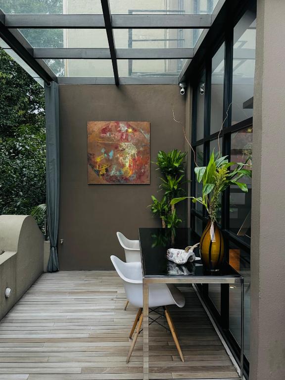 A glass-roofed room with a small desk, chairs, plants and artwork.