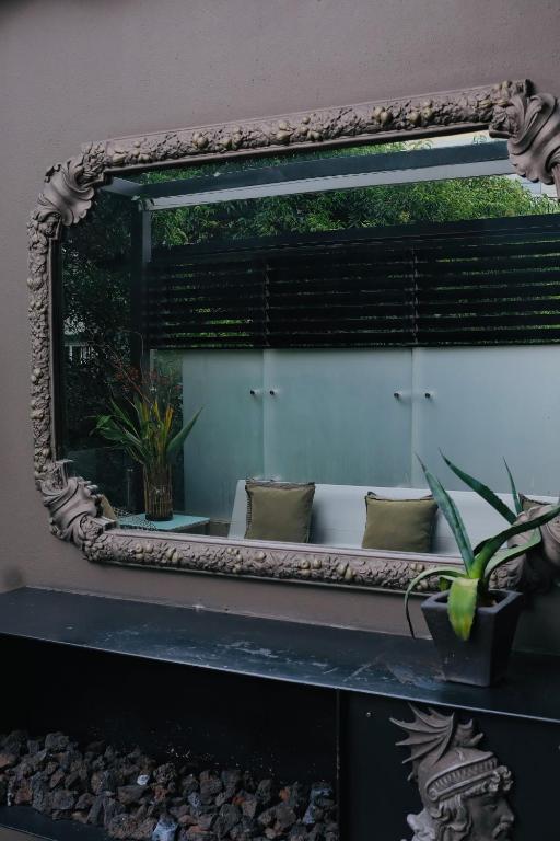 An ornate wall mirror reflects a cushioned lounge and leafy windows beyond.