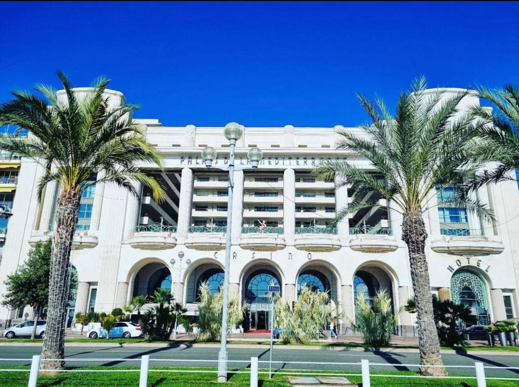 un bâtiment avec des palmiers devant dans l'établissement Le Grand Palais de la Méditerranée Beach Access Apartments - Top Choice In Nice, à Nice