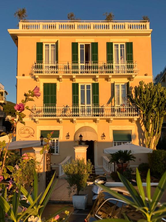 アラッシオにあるHotel Villa Igeaの緑色の窓とバルコニーのある大きな黄色の建物