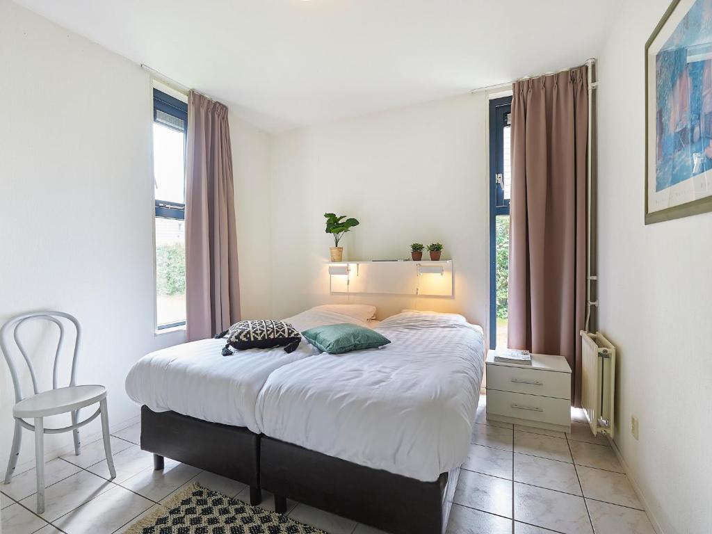 a bedroom with a bed with a chair and windows at Holiday Home in Zeeland near Beaches in Heinkensand