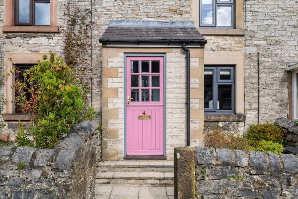 eine rosa Tür an einem Haus mit einer Steinmauer in der Unterkunft Fable Cottage Luxurious Stay in Bakewell