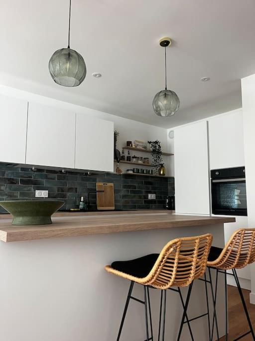 une cuisine avec deux chaises et un comptoir avec des armoires blanches dans l'établissement Appartement Baulois neuf et central, à La Baule
