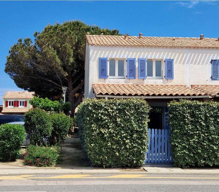 a white house with blue shuttered windows and bushes at MARINA ILE DES PECHEURS in Le Barcarès