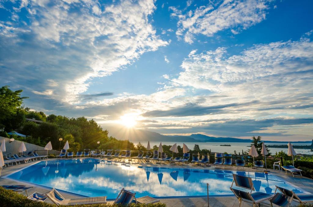 a large swimming pool with chairs and the sun setting at Hotel Belvedere in Manerba del Garda