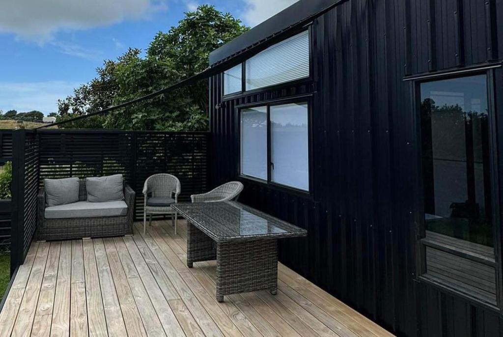 ein schwarzes Haus mit einer Holzterrasse mit einem Tisch und Stühlen in der Unterkunft Fig Cottage in New Plymouth