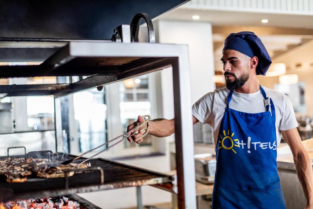 a man in a kitchen preparing food on a grill at Ohtels Carabela in Matalascañas