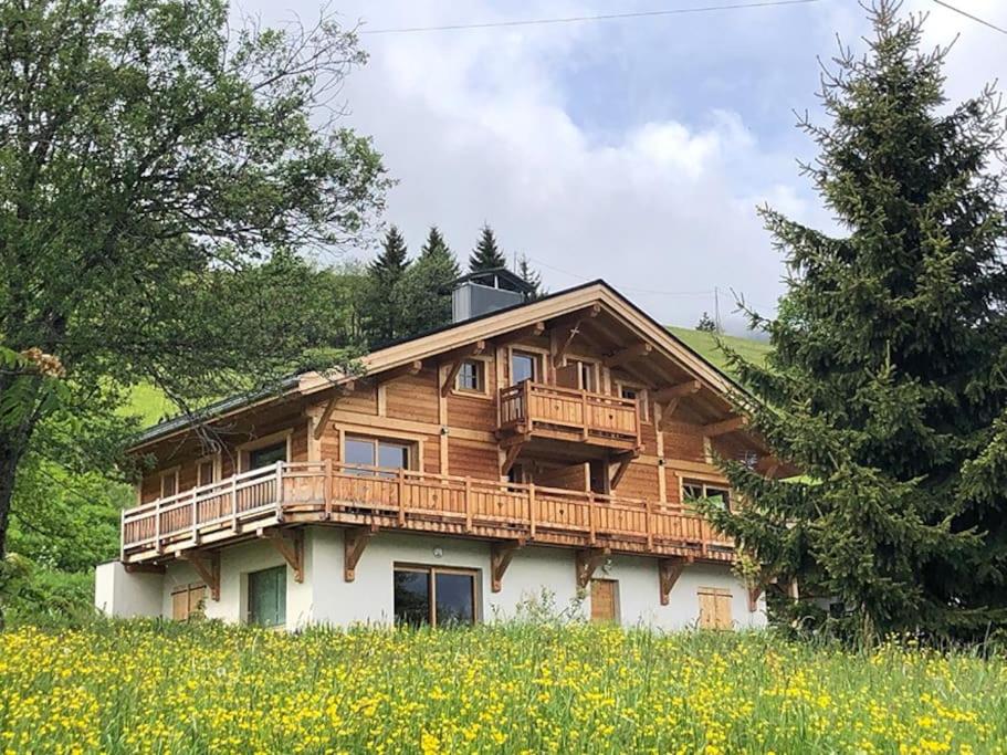une maison en bois avec une terrasse dans un champ de fleurs dans l'établissement L'Arpa - Duplex dans Chalet Neuf - Vue MontBlanc, à Hauteluce
