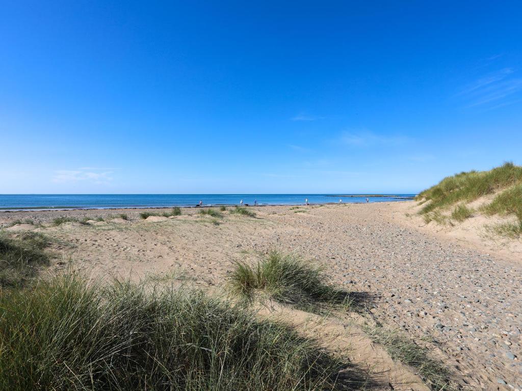 a sandy beach with people walking on the beach at Tides Reach in Rhosneigr