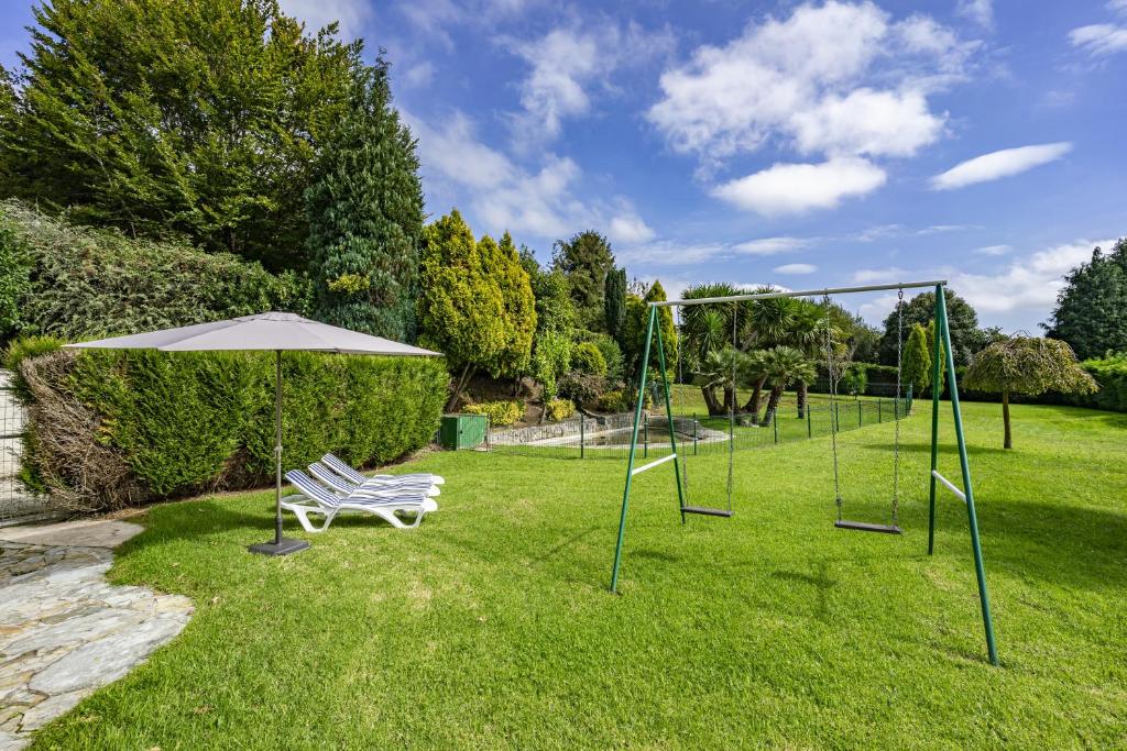 eine Schaukel in einem Park mit einer Bank und einem Sonnenschirm in der Unterkunft Villa de lujo en Cantabria in Puente Arce