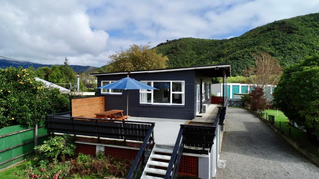 ein blaues kleines Haus mit einer Terrasse und einem Sonnenschirm in der Unterkunft Sounds Good - Waikawa Holiday Home and Berth in Picton