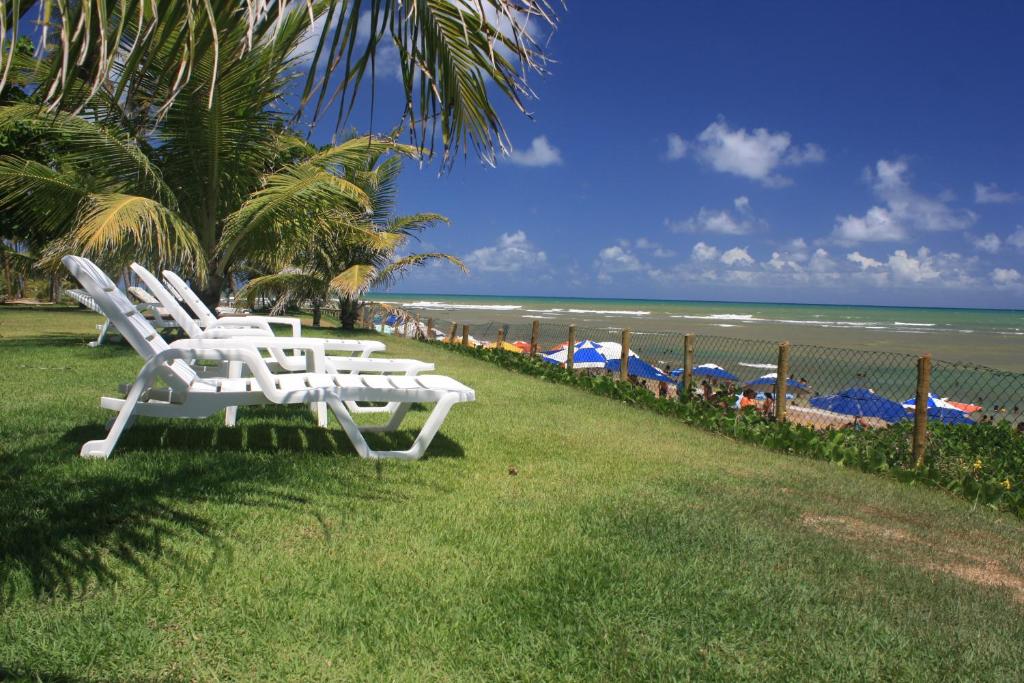 two white chairs sitting on the grass near the beach at Paraíso dos Corais in Guarajuba