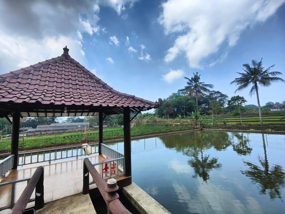 a gazebo next to a pond with palm trees at Padi Loka Villa Kuningan in Koreak