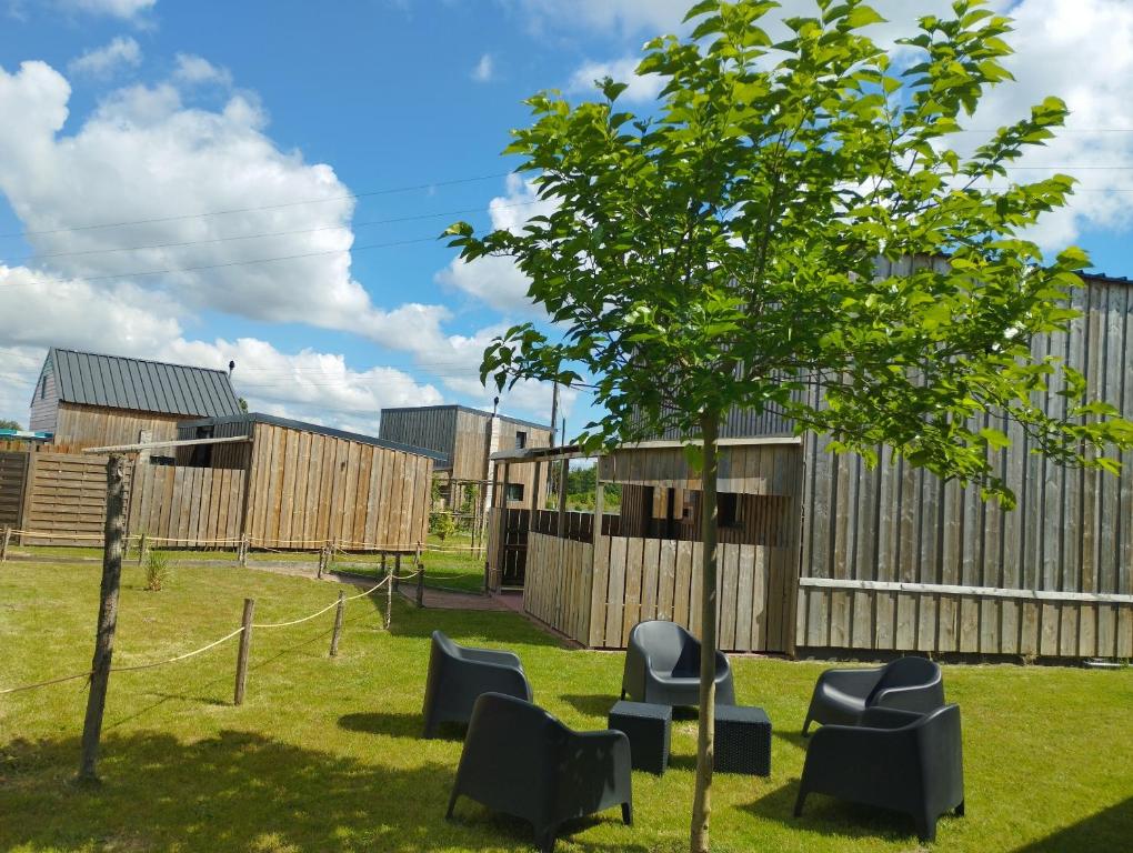 a tree and chairs in a yard with a fence at CHALET CINEMA - Climatisé- Les Belles Ouvrières in Clermont-Créans