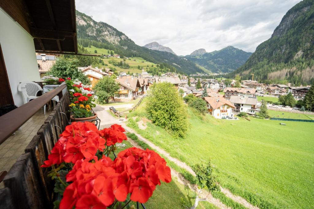 a balcony with red flowers and a view of a town at Cèsa Cherpei - Dog Friendly in Campitello di Fassa