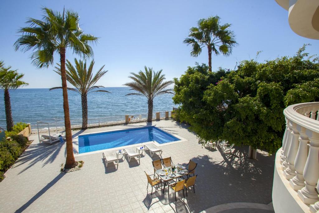a swimming pool next to the ocean with palm trees at Meneou Beachfront Villa Sunset in Pervolia