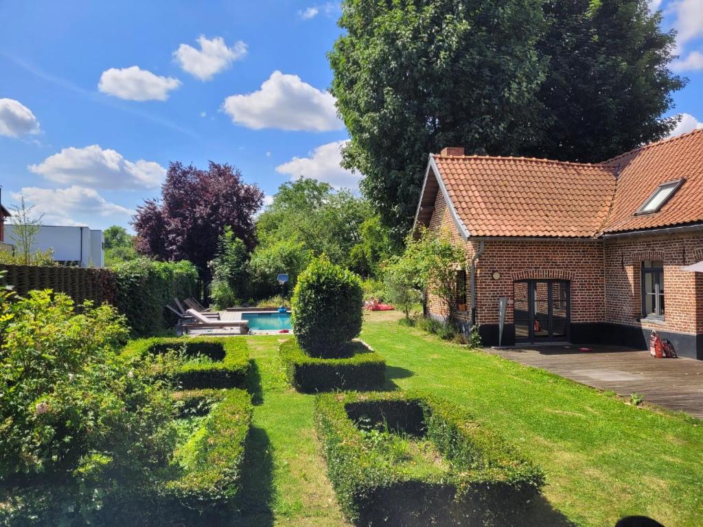 un jardin avec des haies et une maison dans l'établissement ferme de caractère avec piscine et cheminée, à Sainghin-en-Mélantois