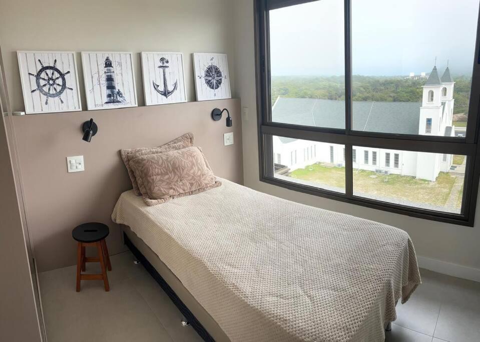 a bedroom with a bed and a large window at Apto Elegante com Localização Privilegiada e Rooftop incrível in Florianópolis