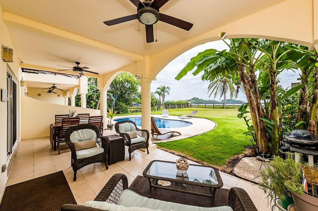 an open patio with a pool and chairs and a ceiling fan at Beachfront Hideaway with Pool & Ocean Views in Playa Flamingo