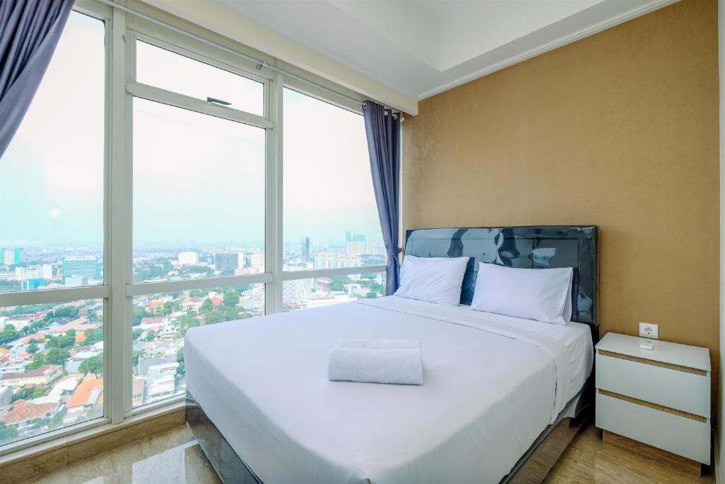 1 cama grande en una habitación con ventanas grandes en Modern Look and Comfy 2BR at Menteng Park Apartment By Travelio, en Yakarta