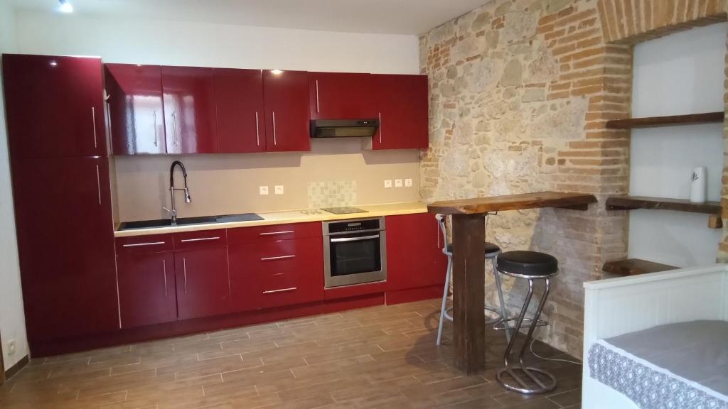 La cuisine est équipée de placards rouges, d'un évier et d'un comptoir. dans l'établissement studio centre Lavaur, à Lavaur