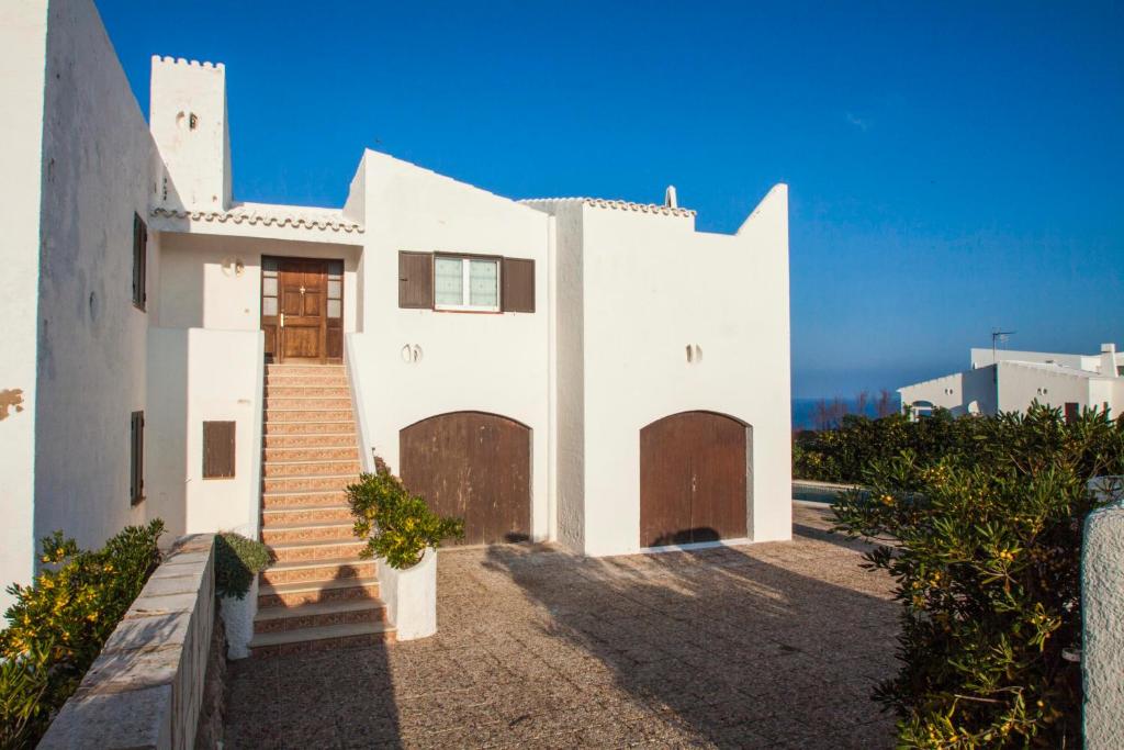 een wit huis met bruine deuren en trappen bij Rocamar 2 in Cala Morell
