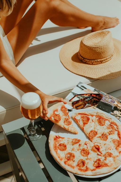 a woman holding a glass of beer next to a pizza at Olé Tropical Tenerife Adults Only in Playa de las Americas