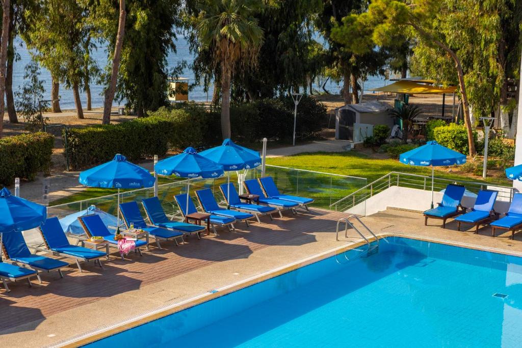 a pool with lounge chairs and blue umbrellas at Park Beach Hotel in Limassol