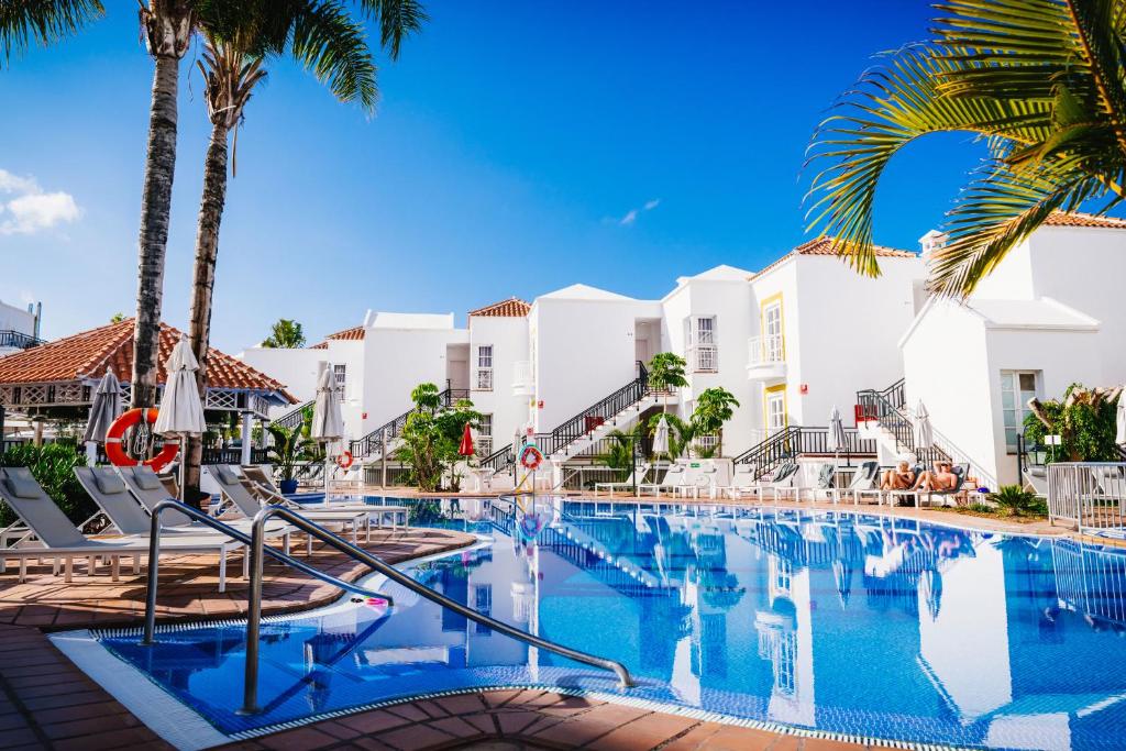 a swimming pool with palm trees and buildings at Apartamentos Parque del Sol in Adeje