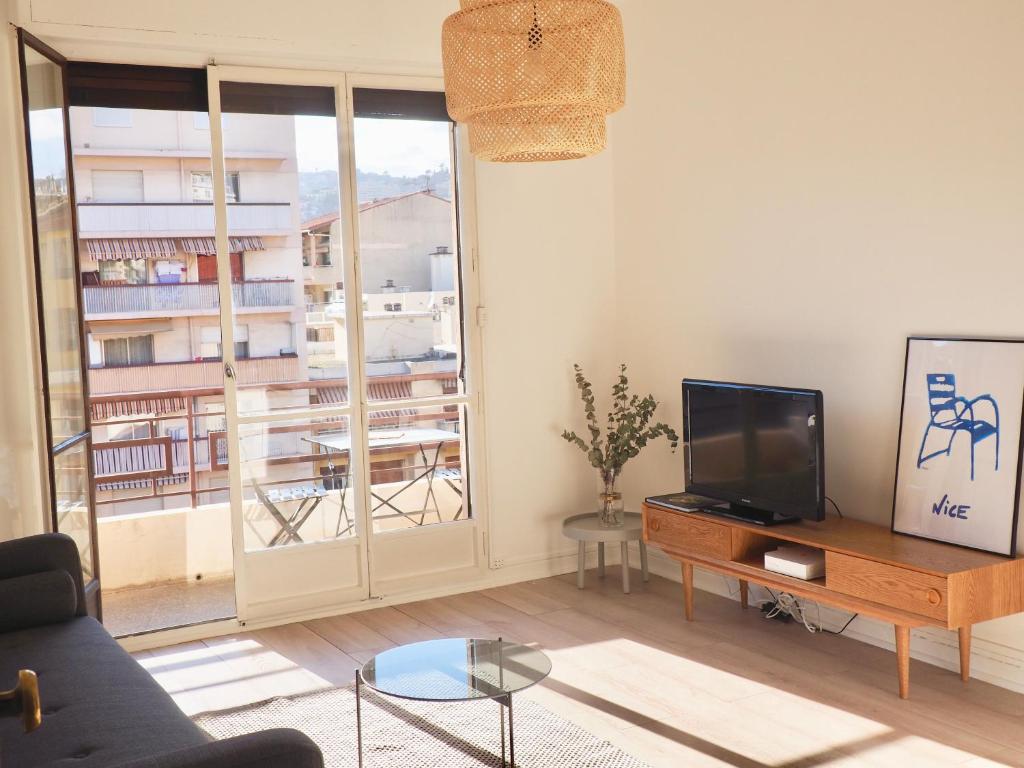 un salon avec une télévision et une grande fenêtre dans l'établissement Appartement proche de Libération avec balcon ensoleillé, à Nice