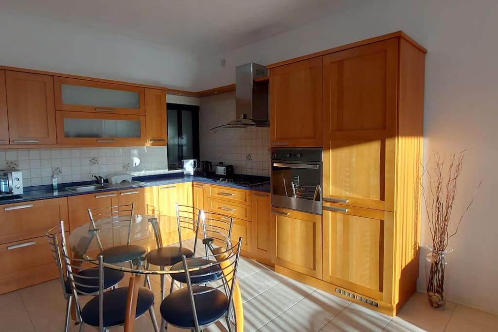 Una cocina con gabinetes de madera y una mesa y sillas. en Birzebbugia - 100m from beach & promenade, en Birżebbuġa
