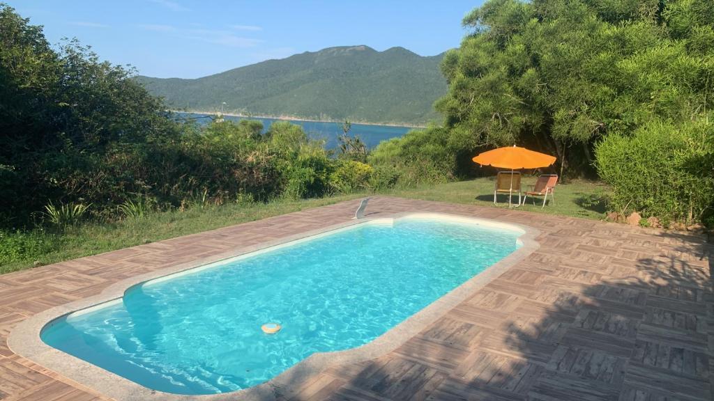 a swimming pool with a table and an umbrella at Bangalô Pontal do Atalaia com piscina para casal ou família in Arraial do Cabo