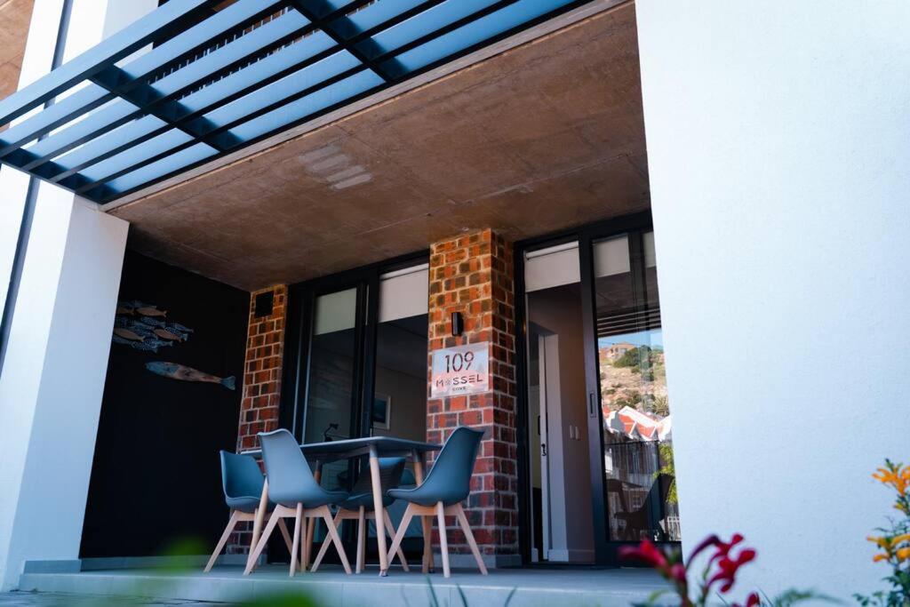 Un patio con una mesa y sillas frente a un edificio. en 109 Mossel Cove Home away from Home, en Mossel Bay